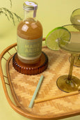 Bottle of Margarita mix on a wooden tray with a glass and lime wedge.