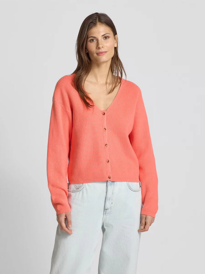 Woman wearing a coral cardigan and light blue jeans on a gray background