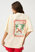 Woman wearing a cream-colored t-shirt with a tropical design and 'Club Tropicana' text on the back.