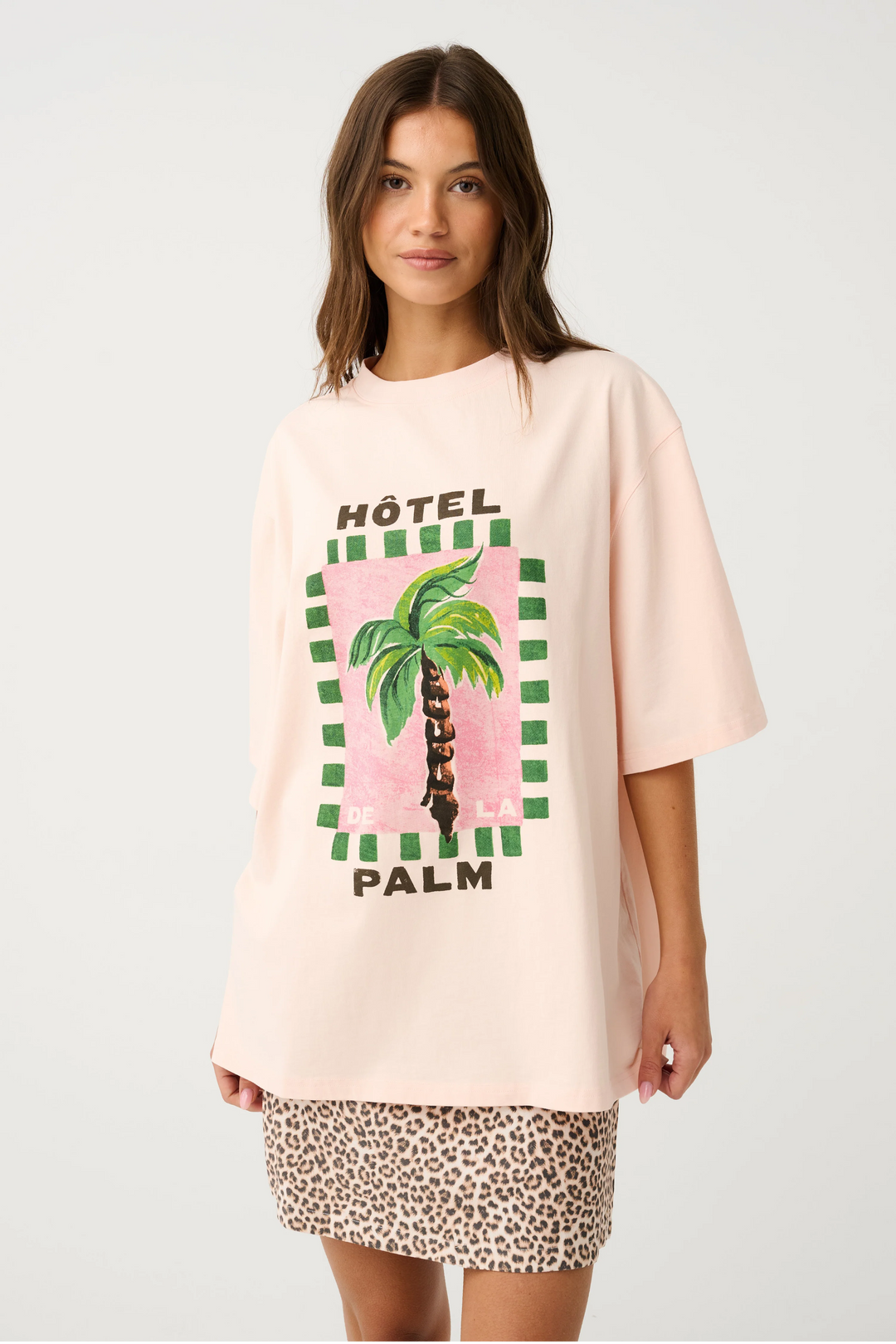 Woman wearing a pink oversized t-shirt with a palm tree design and leopard print shorts on a white background