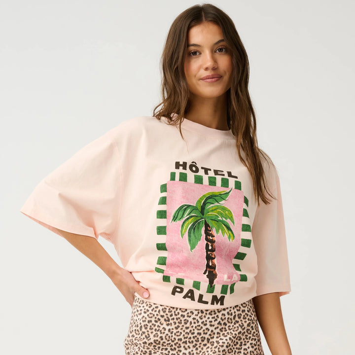 Woman wearing a pink graphic t-shirt with palm tree design and leopard print skirt on a white background