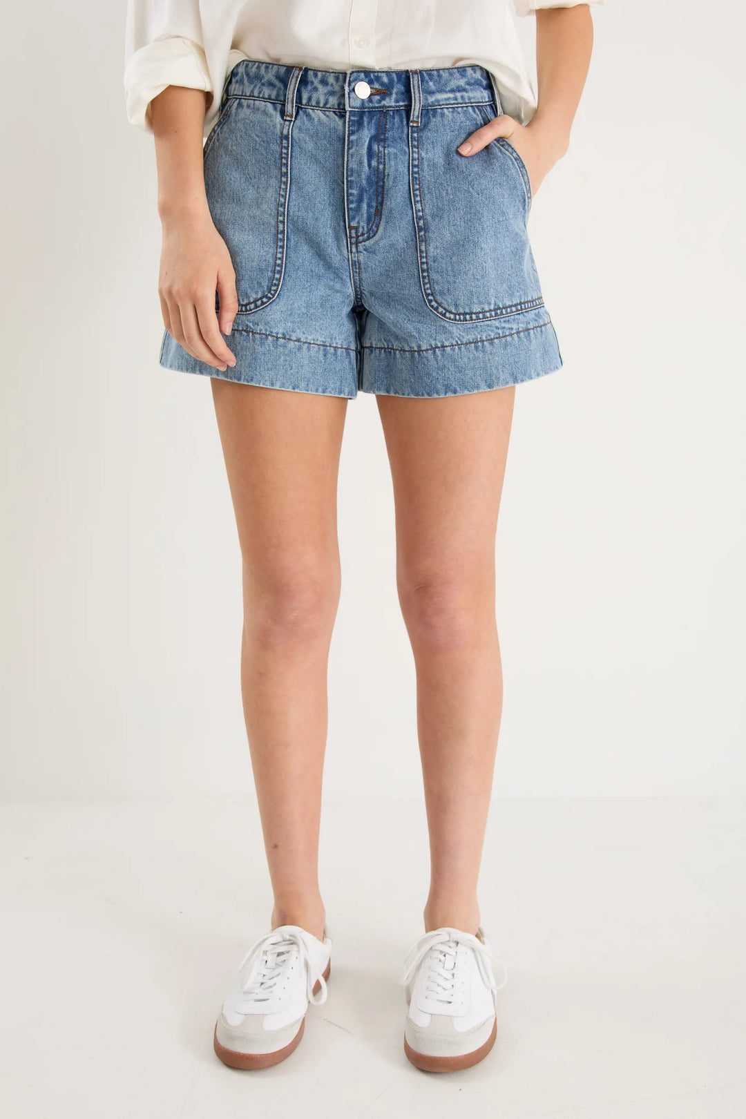 Person wearing blue denim shorts and white sneakers on a plain background