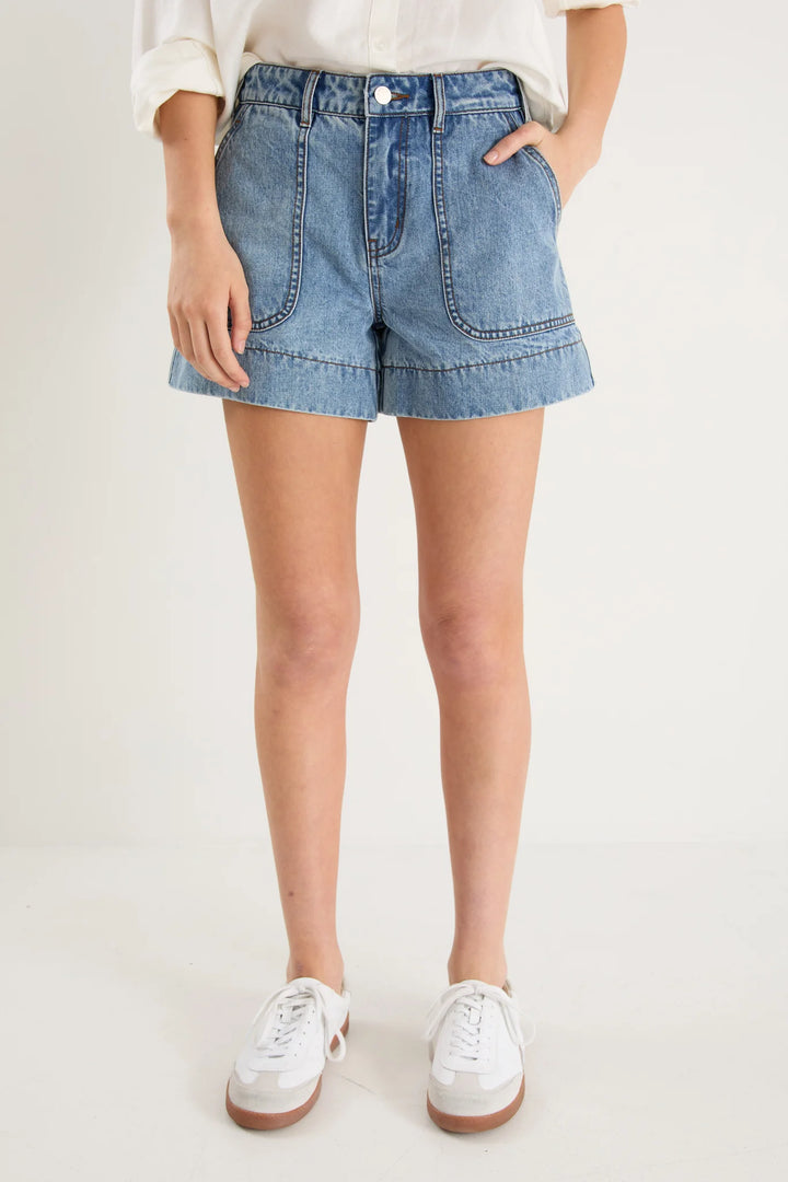 Person wearing blue denim shorts and white sneakers on a plain background