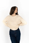 Woman wearing a beige sweater and dark jeans on a white background
