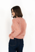 Woman wearing a pink sweater and dark jeans on a white background