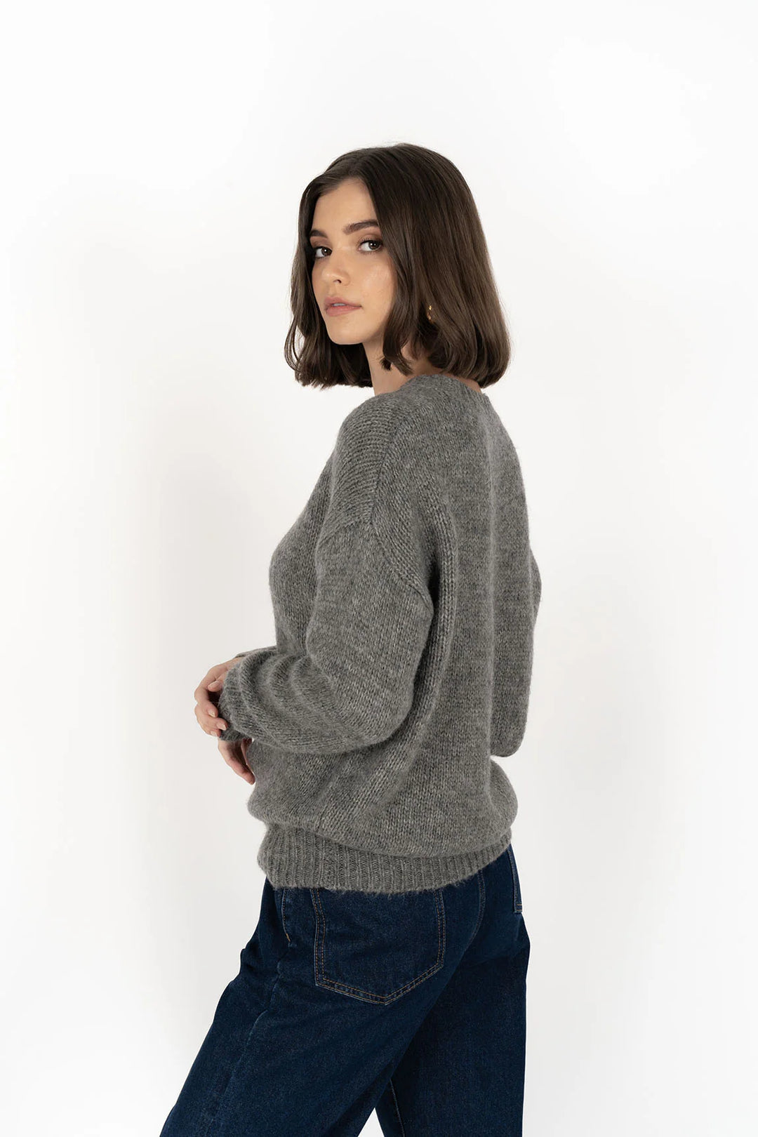 Woman wearing a gray sweater and dark jeans on a white background
