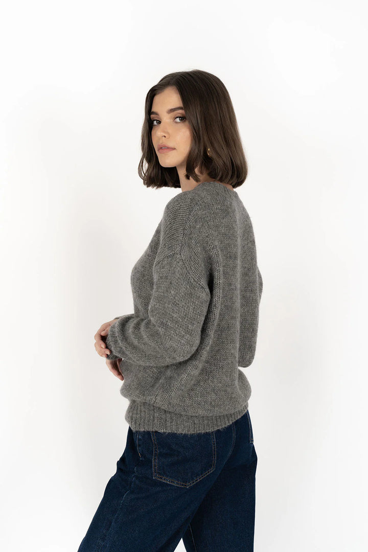 Woman wearing a gray sweater and dark jeans on a white background