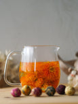 Glass teapot with orange liquid and flowers on a wooden surface