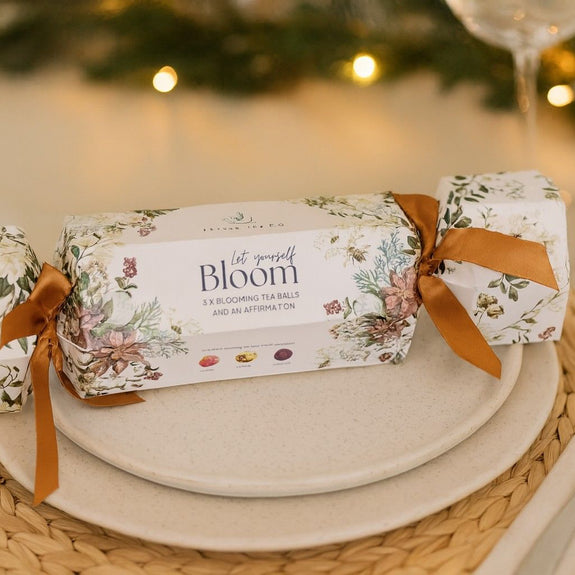 Christmas cracker with floral design and 'Bloom' tea ball on a table setting.