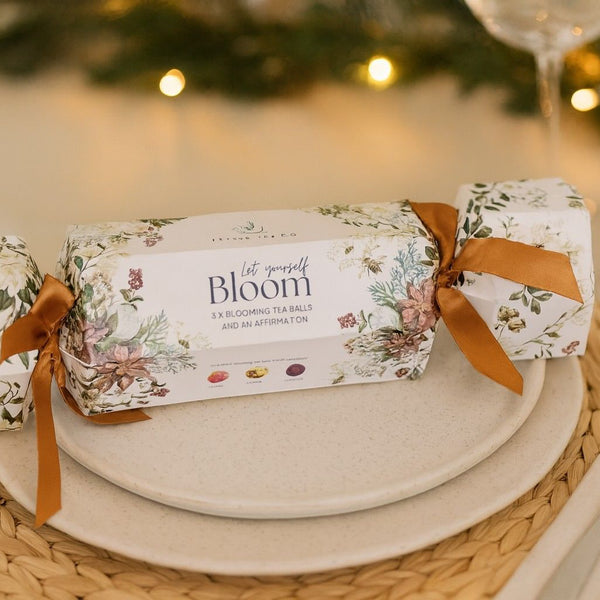 Christmas cracker with floral design and 'Bloom' tea ball on a table setting.