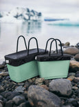 Two green storage bins with black lids on a rocky beach.