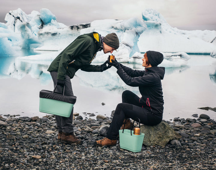 Two people with green coolers by a glacier