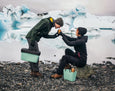 Two people with green coolers by a glacier