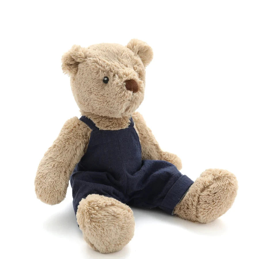 Plush teddy bear wearing navy blue overalls on a white background