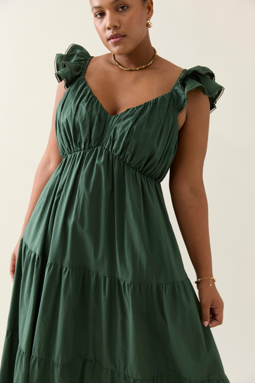 Woman wearing a green isle of mine dress with ruffled shoulders against a neutral background