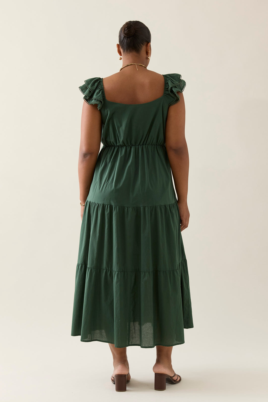 Woman wearing a green isle of mine dress with ruffled sleeves on a plain background