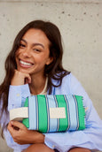 Woman holding a green and blue striped clutch against a neutral background
