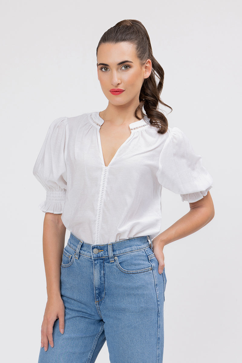 Woman wearing a white addyson blouse and blue jeans on a plain background