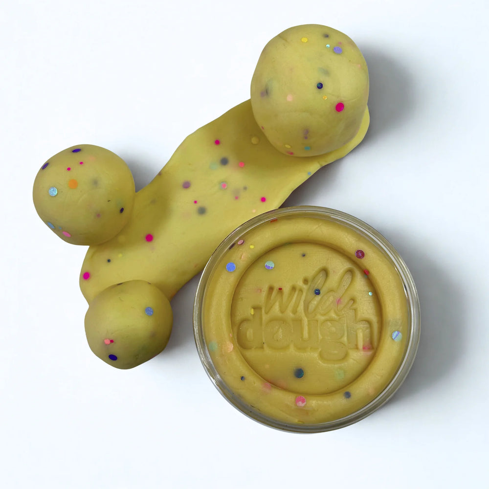 Yellow play dough with colorful sprinkles and a container labeled 'wild dough' on a white background