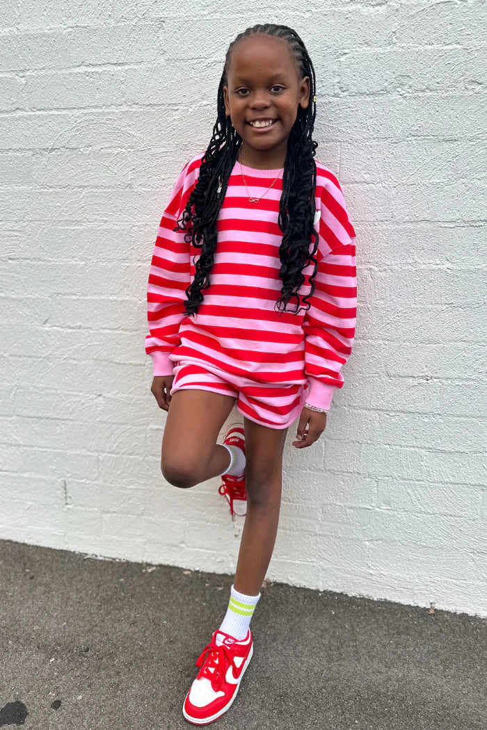 Child wearing a red and white striped outfit against a white brick wall.