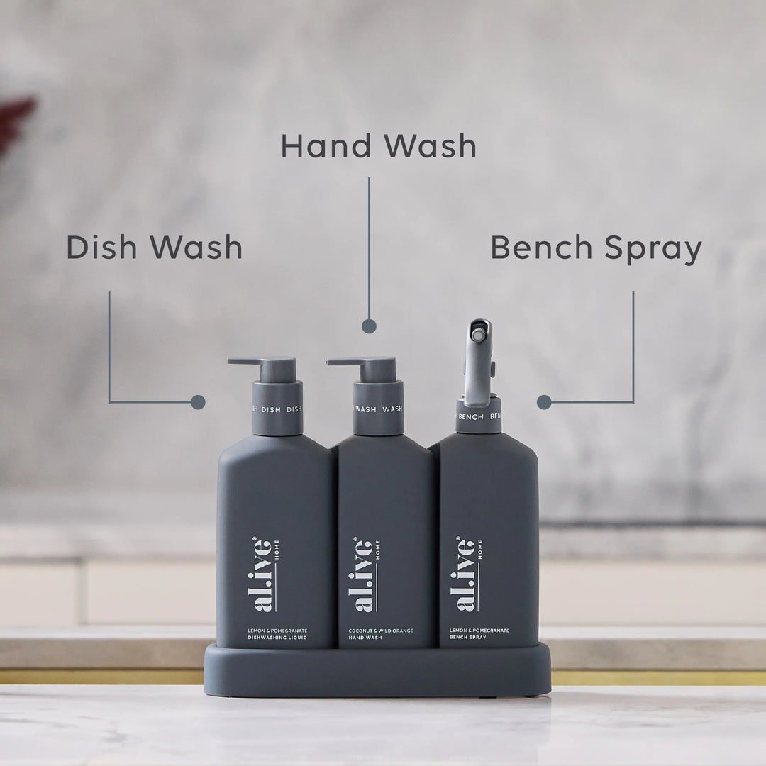 Three gray bottles labeled 'Hand Wash', 'Dish Wash', and 'Bench Spray' on a stand with a blurred background.