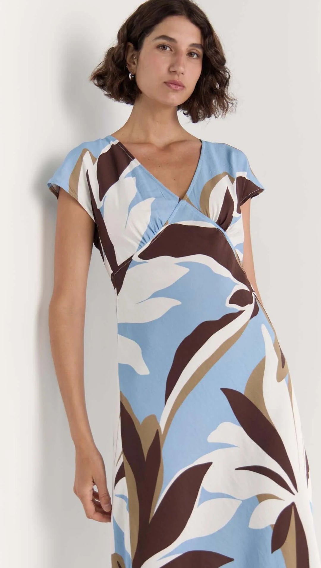 Woman wearing a floral dress with brown, white, and blue pattern on a plain background