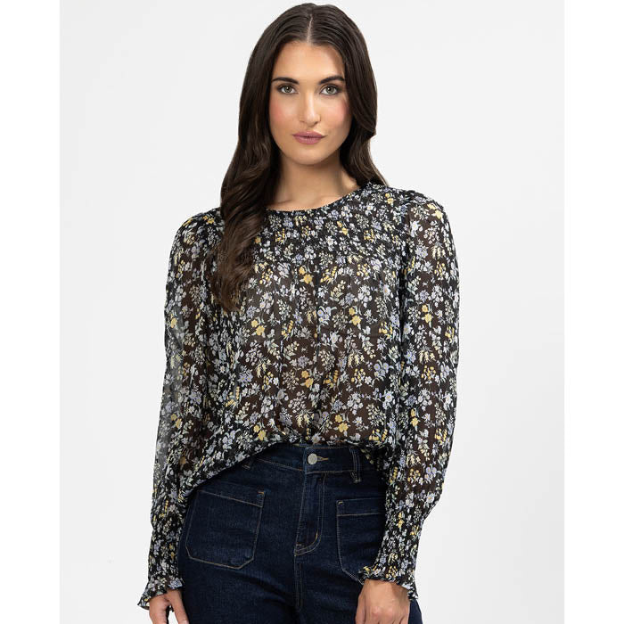 Woman wearing a floral hug me blouse and dark jeans on a white background