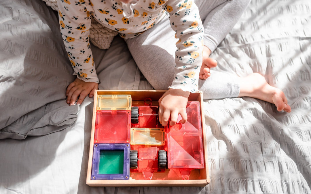 Child playing with a connetix colorful transparent box on a bed