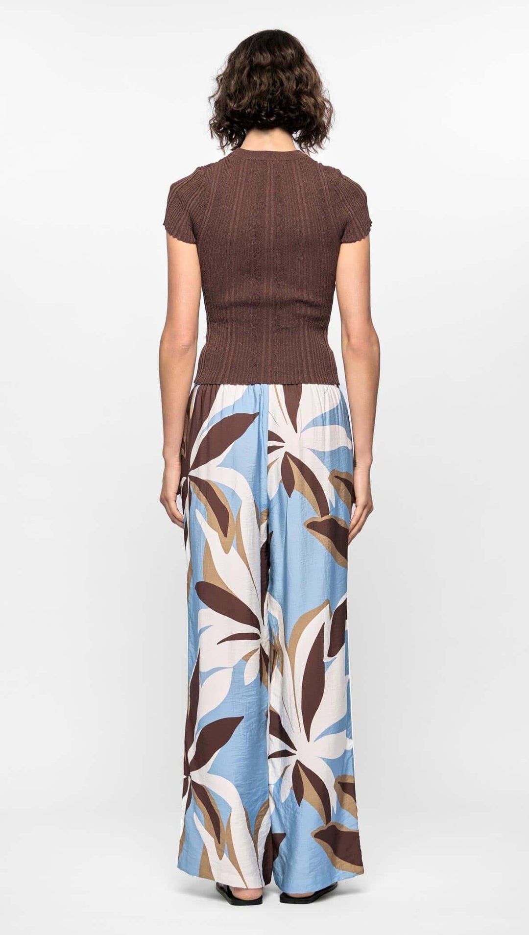 Woman wearing a brown top and long floral skirt on a white background