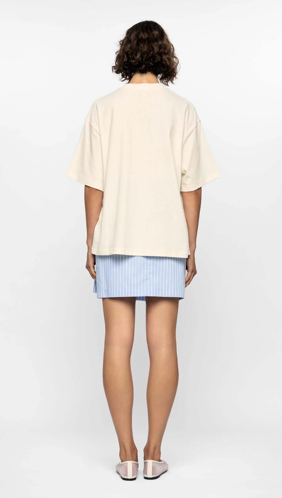 Person wearing a beige top and blue checkered shorts on a white background