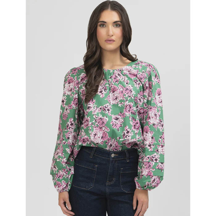 Woman wearing a floral blouse with green and pink flowers on a plain background