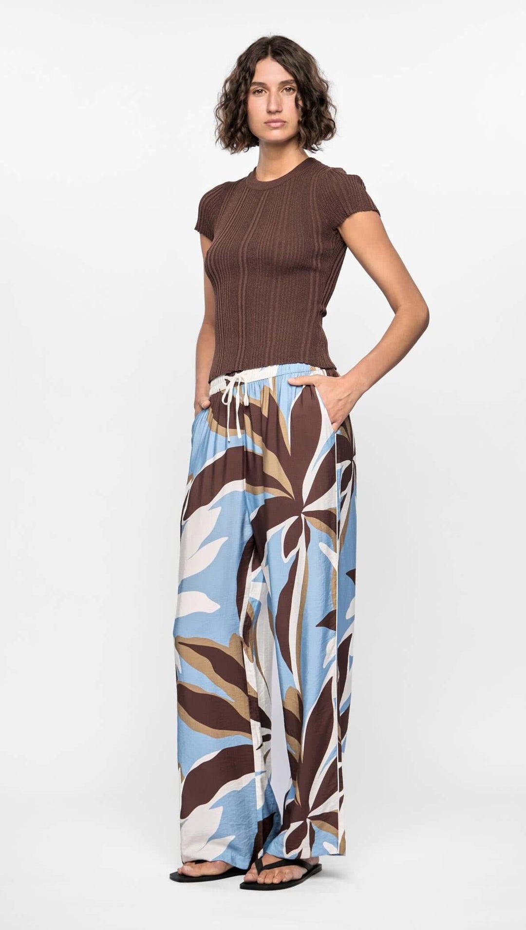 Woman wearing a brown top and patterned wide-leg pants on a white background