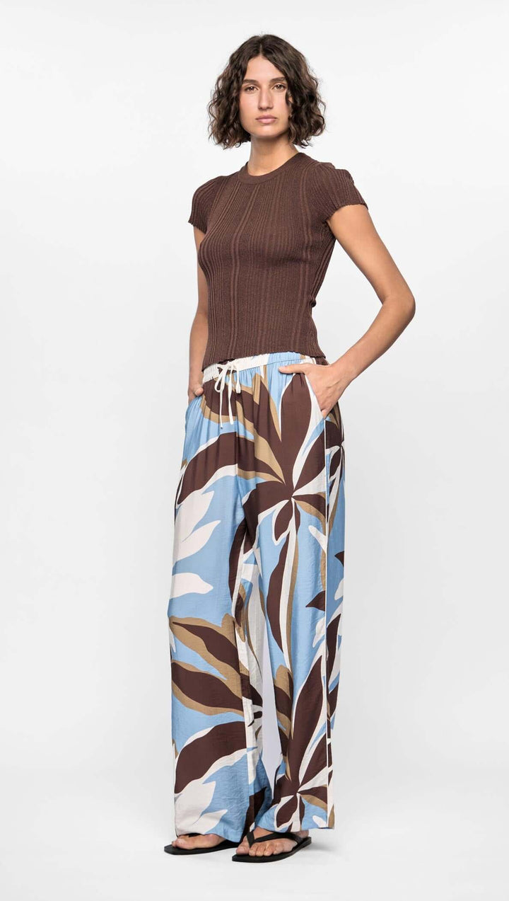 Woman wearing a brown top and patterned wide-leg pants on a white background