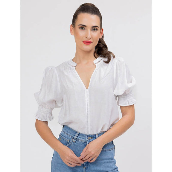 Woman wearing a white addyson blouse with short sleeves and blue jeans on a light gray background