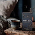 Tea cup and 'Good Night' tea box on a wooden surface with a blurred background