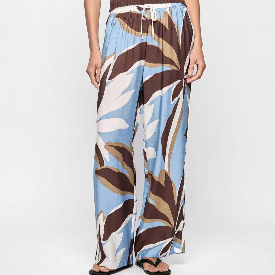 Woman wearing a brown top and patterned blue and brown pants on a white background