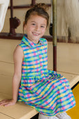 Young girl wearing a colorful checkered dress sitting on a wooden bench.
