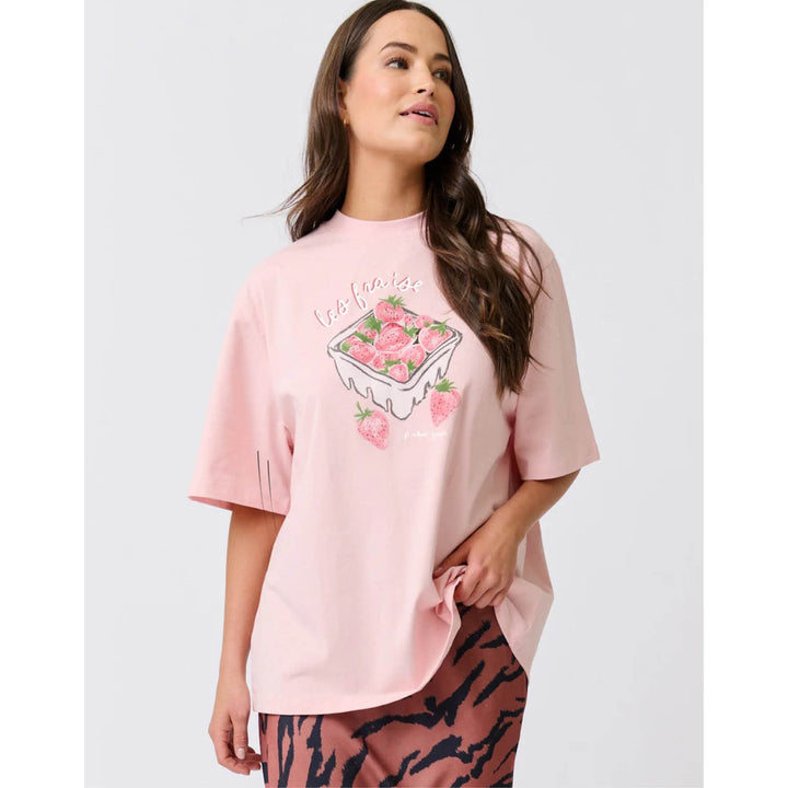 Woman wearing a pink oversized t-shirt with a graphic design on a plain background