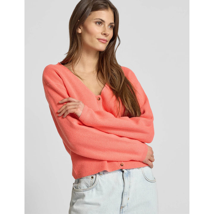 Woman wearing a coral sweater and light blue jeans on a plain background