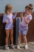 Two young girls in matching outfits standing on a wooden deck.