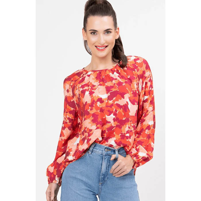 Woman wearing a red and orange united floral blouse with blue jeans on a white background