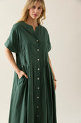 Woman wearing a green isle of mine dress with buttons on a plain background