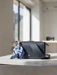 Black handbag with a blue and white scarf on a marble surface with large windows in the background