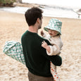 Man holding a child on a beach with a checkered bag