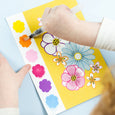Colorful flower stickers on a yellow mat with a child's hand using a marker.