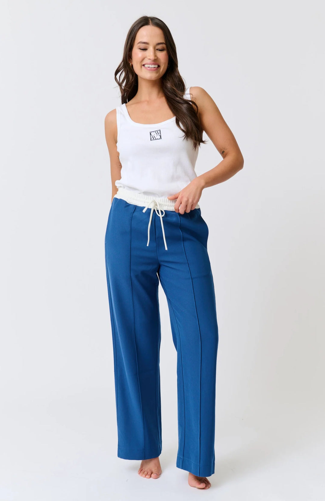 Woman wearing a white tank top and blue pants on a white background