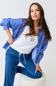 Woman wearing a blue and white striped shirt over a white top with blue pants on a white background