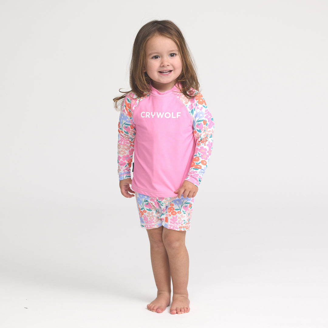 Child wearing a pink 'Crywolf' rash vest with floral sleeves and shorts on a white background