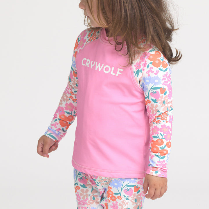 Child wearing a pink 'Crywolf' rash vest with floral sleeves and pants on a white background