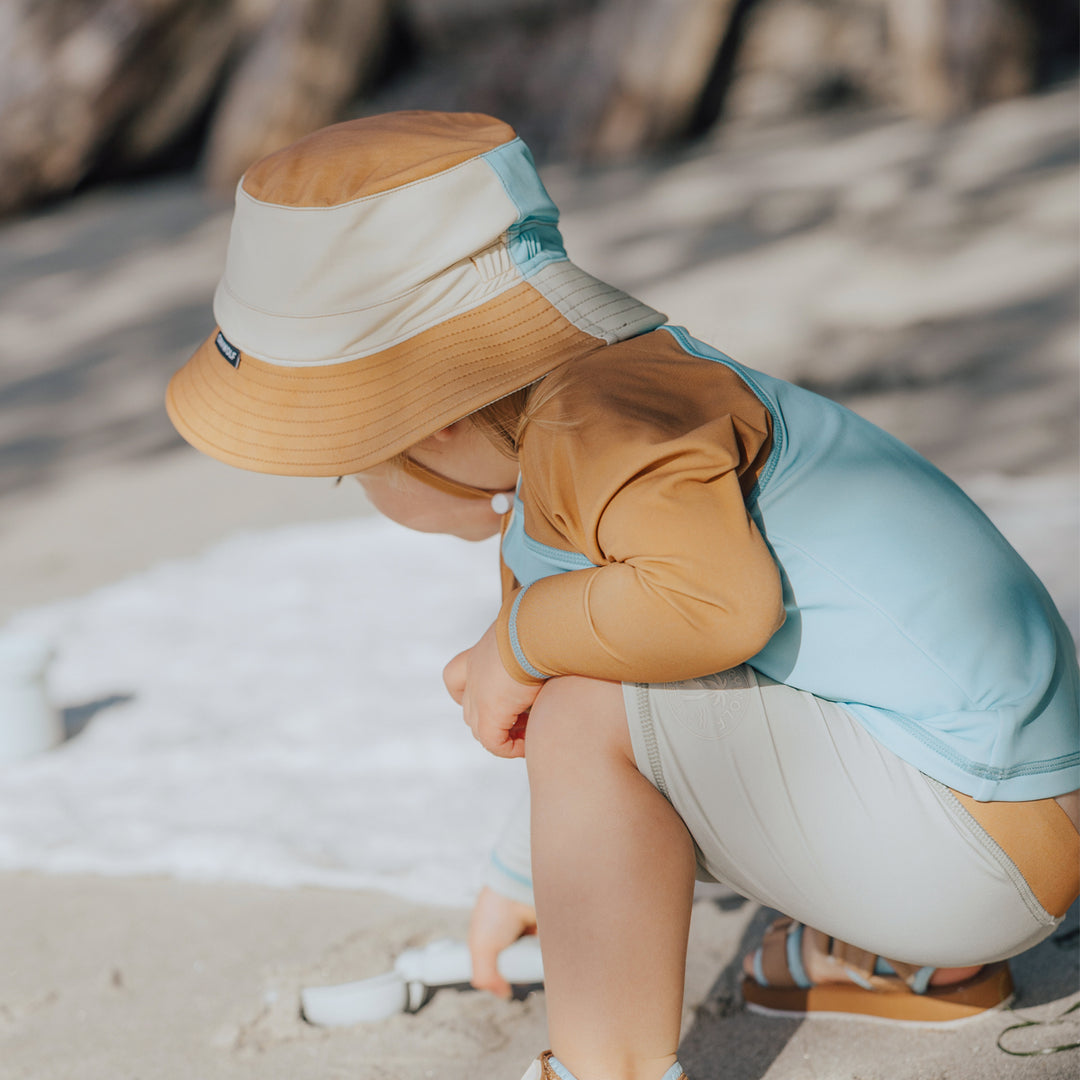Child wearing a colorful hat and sitting on a beach